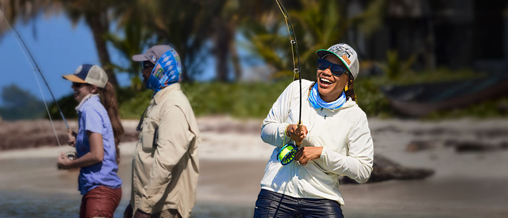 Several anglers smile while knee-deep in the ocean fly fish in the tropics.