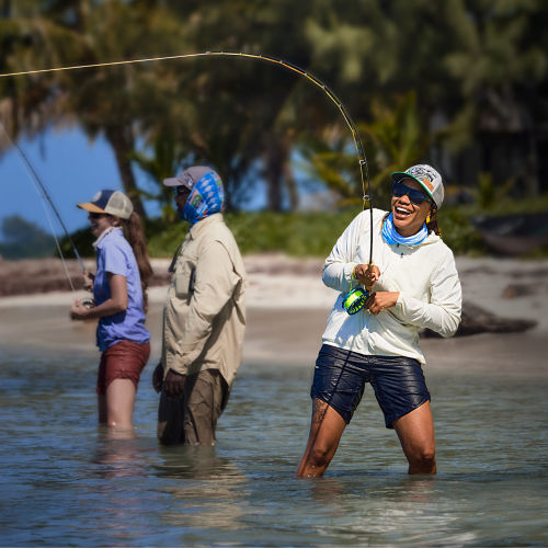 An angler reeling in a fish with a big smile on her face.