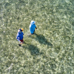Two anglers, seen from above, walk in shallow ocean water.