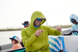 An angler wearing a PRO Sun hoodie measures out some line while holding the end in their teeth.
