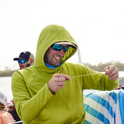 An angler wearing a PRO Sun hoodie measures out some line while holding the end in their teeth.
