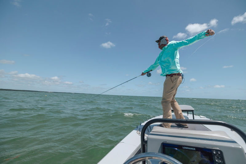 An angler pulls his line back as he casts from the bow of a small vessel.