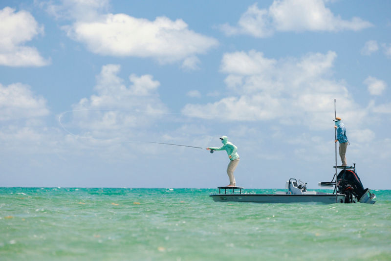 An angler casts his fly rod from the front platform of a skiff.