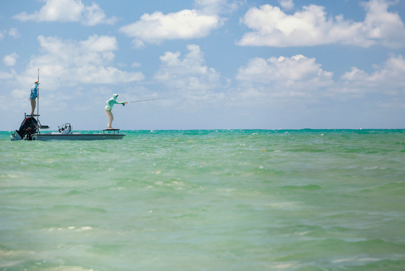 An angler casts off the front of a boat in tropical waters.