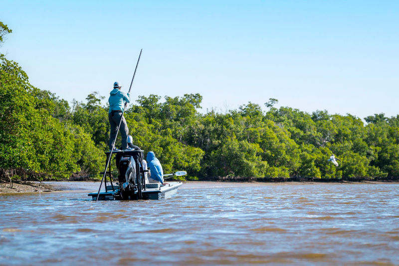 Three people poling a boat along a river bank