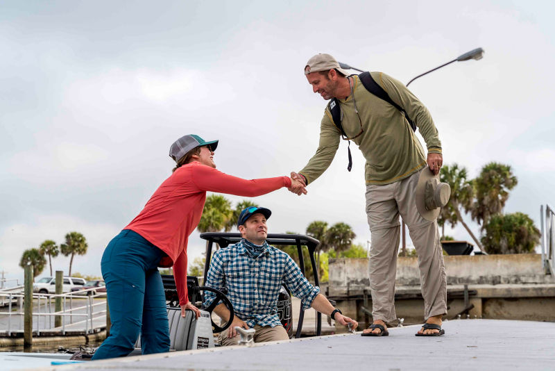 Two people in a boat greet a fellow angler on a dock