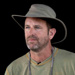 A headshot of Lawrence Glenn wearing a khaki explorer hat