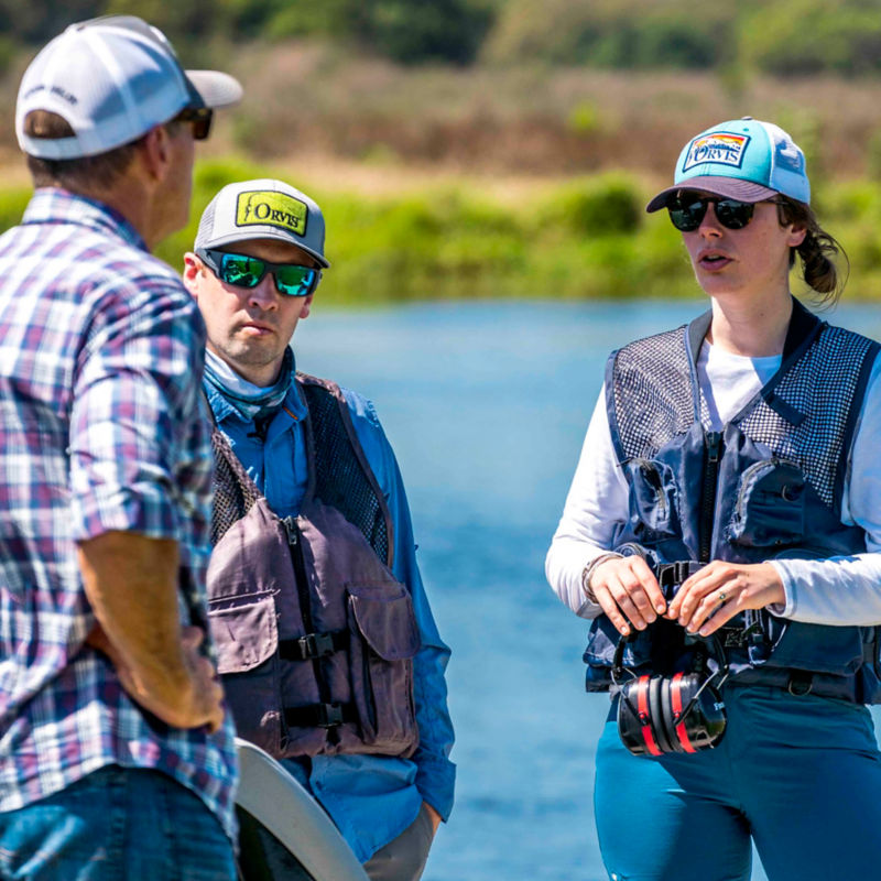Three people talking on the banks of a river