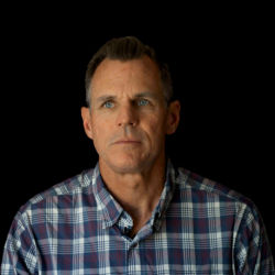 A headshot of Mike Cheek wearing a plaid shirt