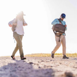 A man and a woman walking in the sunshine with backpacks on