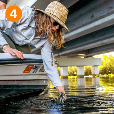 A person tests water from a boat under the Tamiami Trail Bridge