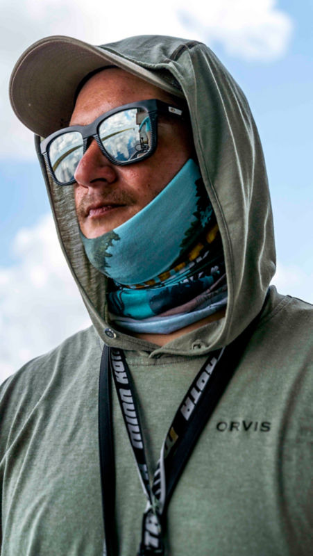 A close up on a man wearing a hood, buff, and polarized sunglasses