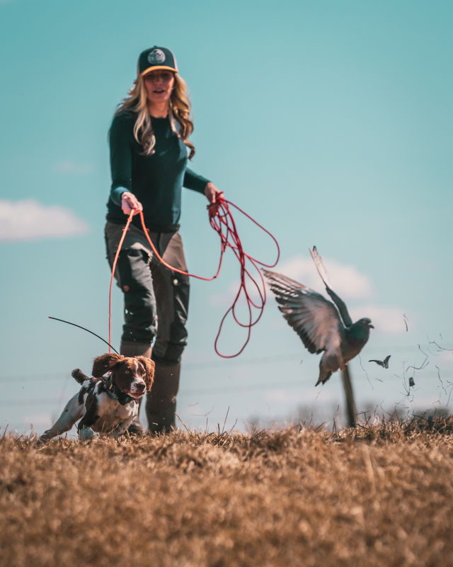 A woman holds the leash of a dog charging after a bird