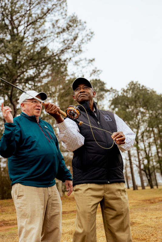 A student pulls their fly rod back for a cast while an instructor watches.