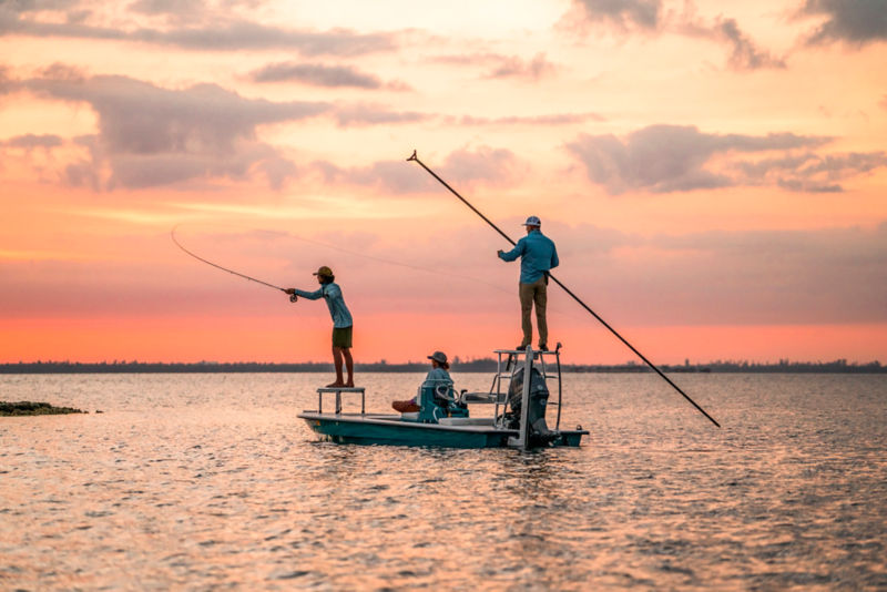 An angler casts from the front of a skiff while another poles from the back.