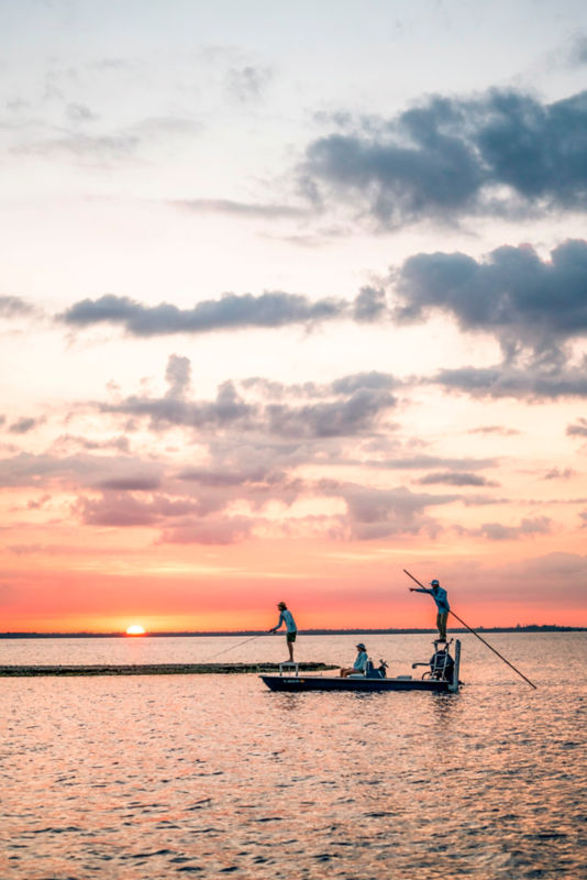 A skiff with three anglers out on the water at sunrise.