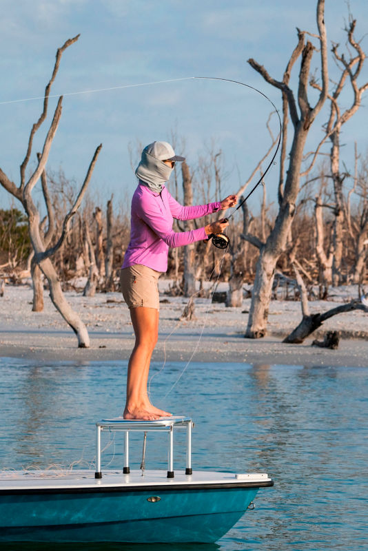 An angler in sunglasses and PRO quarter-zip casts from the front of a skiff.