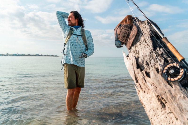 An angler standing ankle-deep in the ocean looks back over his shoulder.