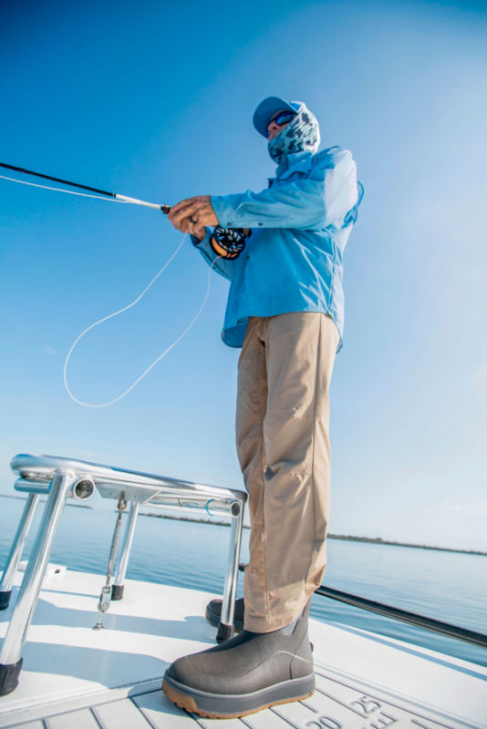 A man wearing a sun protective buff fly fishing from a boat.
