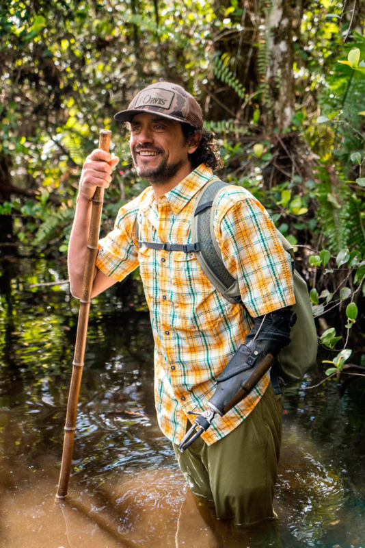 A man is wading through a swamp with a guide stick.