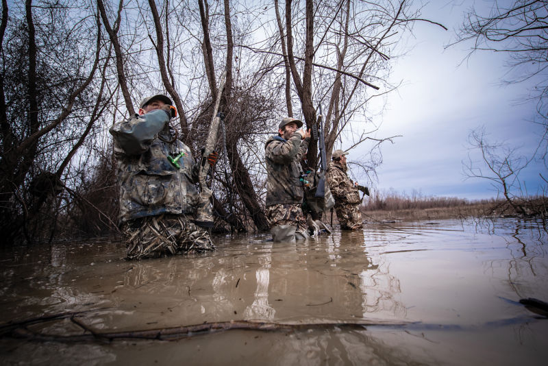 Three hunters wade through knee-deep water