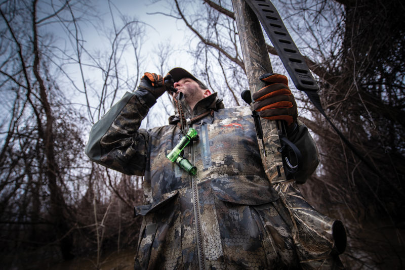 A hunter in camouflage blows a bird call.