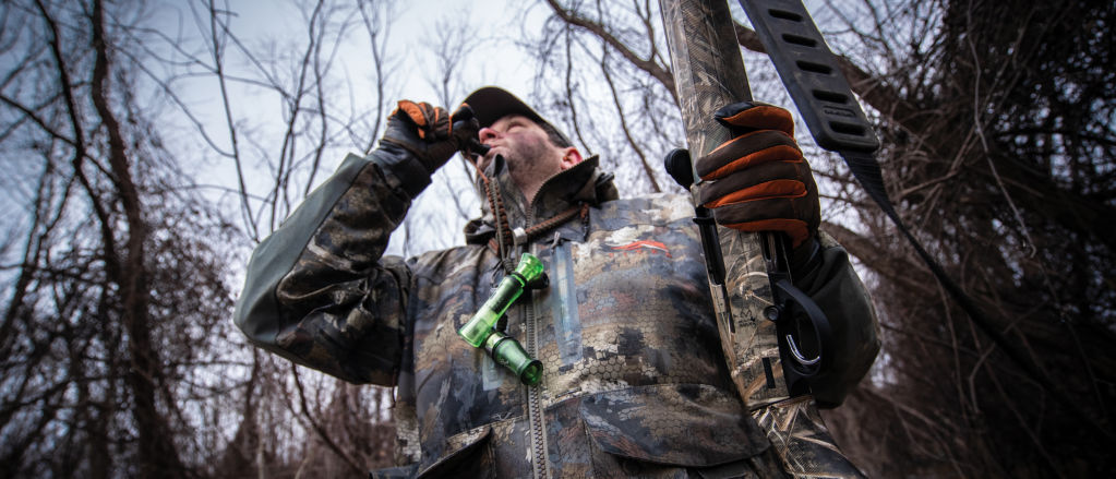A hunter in camouflage blows a bird call.