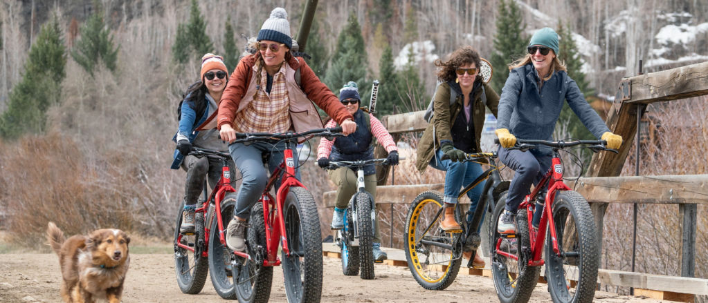 A group of women riding fat tire bicycles down a dirt road on a cold fall day