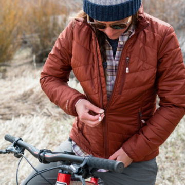 Woman zips up her Recycled Drift Vest as she sits on her bike during a cold day.