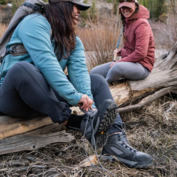 A couple of anglers adjust their wading boots on a fallen tree trunk.