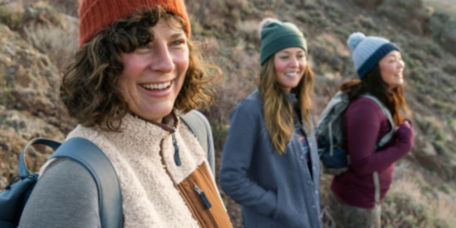 Three women wear layers to go out on a mountainous hike