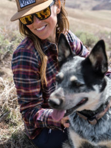 A woman wearing a flannel shirt smiling while petting a dog