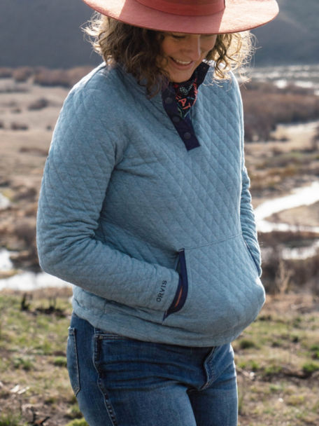 Woman in Outdoor Quilted Snap Sweatshirt warms her hands in her front pockets as she overlooks a widning riverbank.