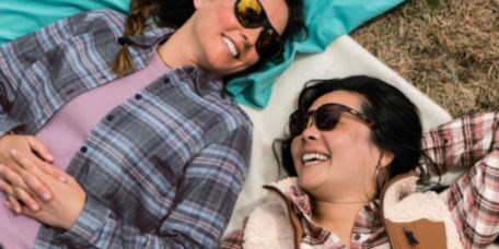 Two people smiling in sunglasses while laying on the grass