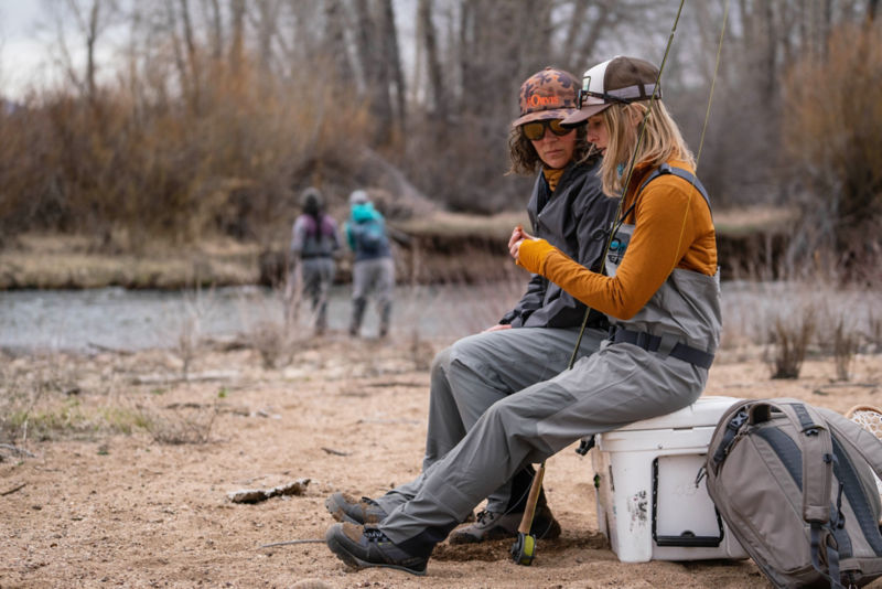 Two women beachside tying flies on the line.