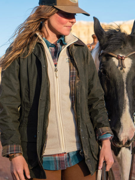 Woman in Barbour Classic Beadnell and R65 Sweater Fleece Vest tends to her horse.