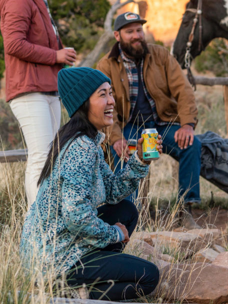 Woman in Mineral Blue Current Print Outdoor Quilted Snap Sweatshirt socializes with her firends by a campfire on a ranch.