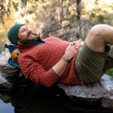 Man in Outdoor Quilted Snap Sweatshirt lays back on some rocks next to a shallow pool.