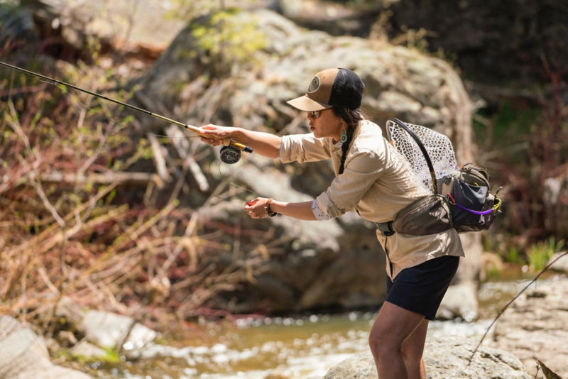 Angler casts line in the middle of a woodland river.