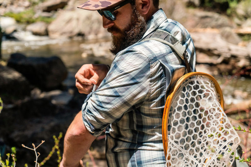 Angler adjusts his shirt along a rocky pool of water.