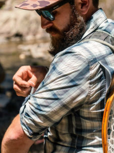 An angler rolls up his sleeves on a plaid button-down shirt.