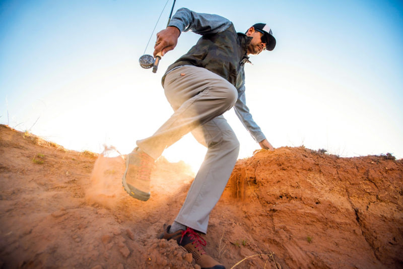 Angler hops down a rocky dune towards a river.