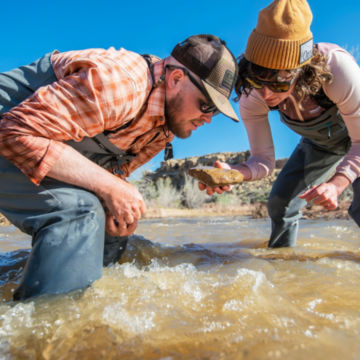 A couple of anglers inspect a rock from a muddy river.