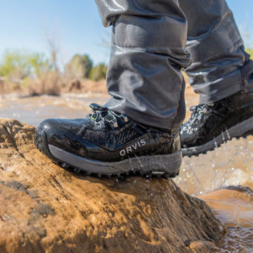 Woman in Ultralight wading boots walks out of a river onto a rock.