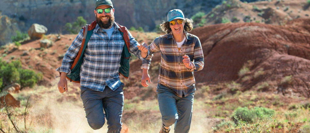 Two smiling hikers in flannel shirts race down a red dirt hill