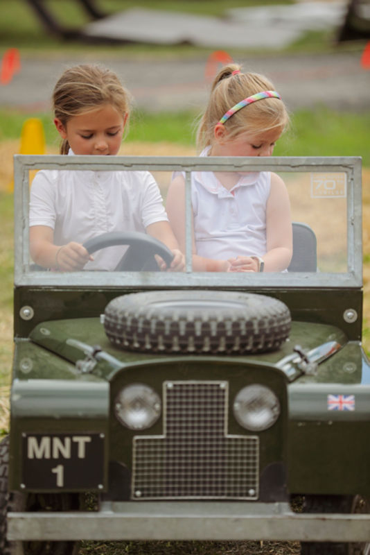 Two little girls driving a model land rover through a course.