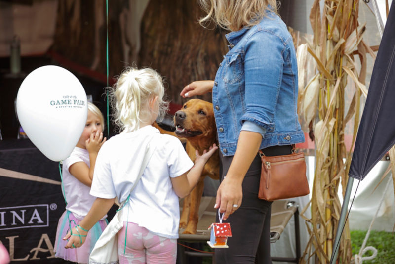 Two little girls with a Game Fair balloon petting a dog.