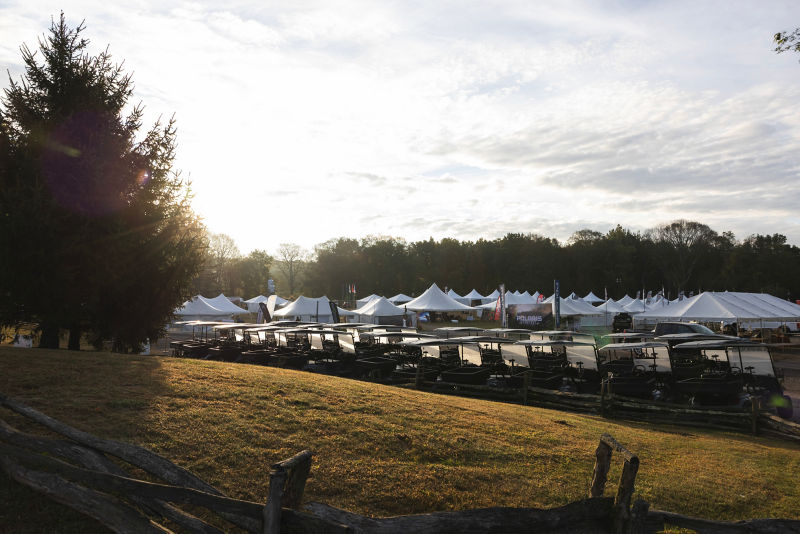 A line of golf carts parked in front of waiting tents at dawn.