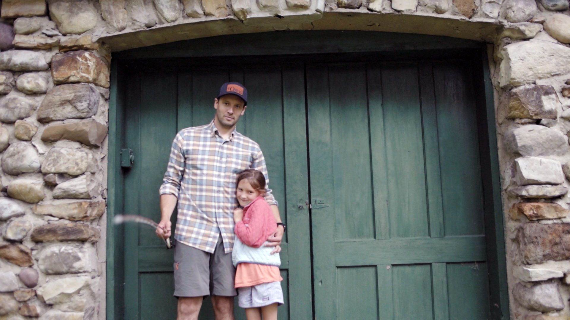 Simon Perkins and his small daughter coy up for the photographer in front of green double doors in a rough stone building