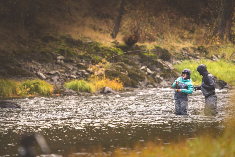 Two anglers share a laugh while wading knee deep in the river.